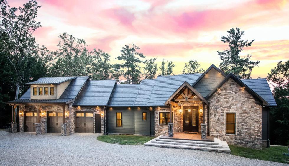 Photo of timber frame home with stone and wood exterior and three car garage bay attached to the home by an enclosed breezeway. Photo taken at sunset