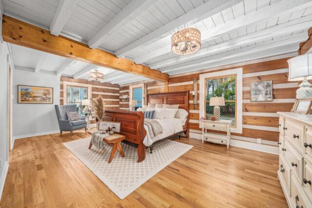 Photo of a bedroom in a wide chink log home. With bright white painted wood ceilings and the bright white chink in the exterior walls, the bedroom feel airy and light. The floors are a light wood.