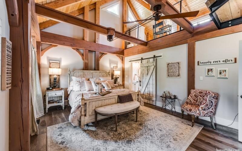 Photo of master bedroom with loft area above the bedroom, wood ceiling and a-frame trusses and a dark hardwood floor